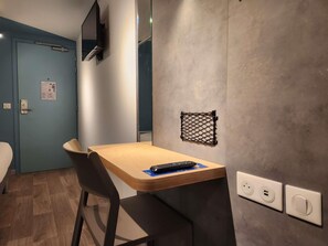A small room with a wooden table, a chair, a TV mounted on the wall, and a power outlet. - ibis budget Chambourcy Saint-Germain (Chambourcy)