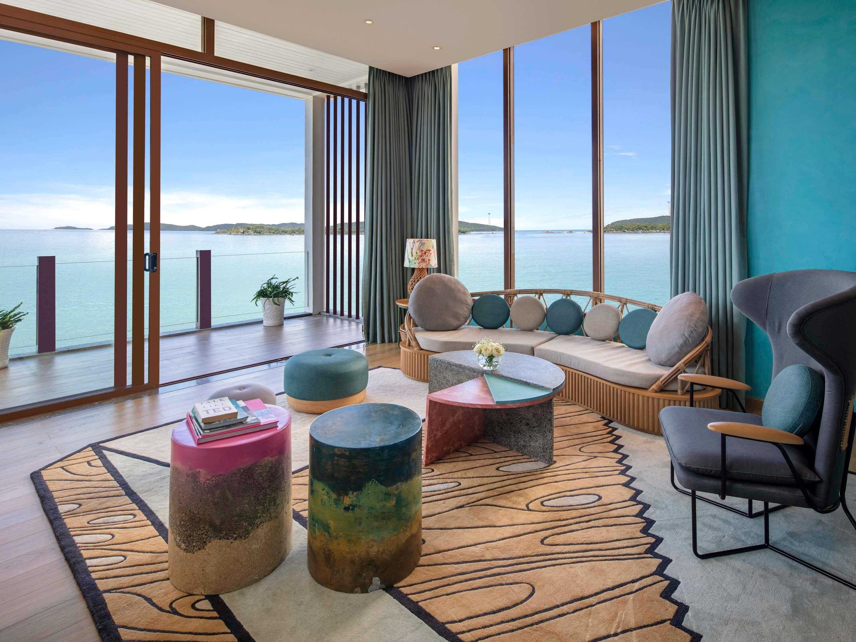 A modern living room with a large window overlooking a body of water, a sofa set, and two round coffee tables.