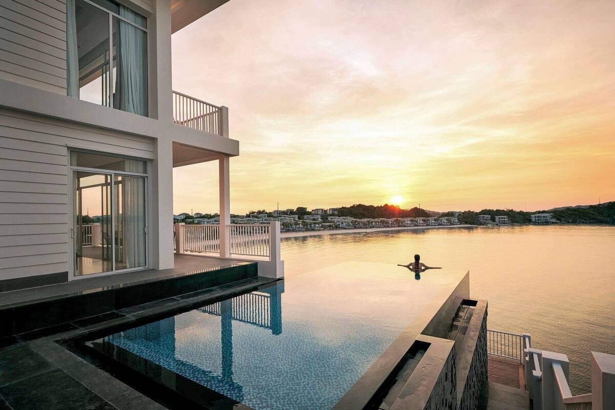 Ein modernes Gebäude mit Pool, Balkon und Blick auf den Sonnenuntergang über dem Wasser.