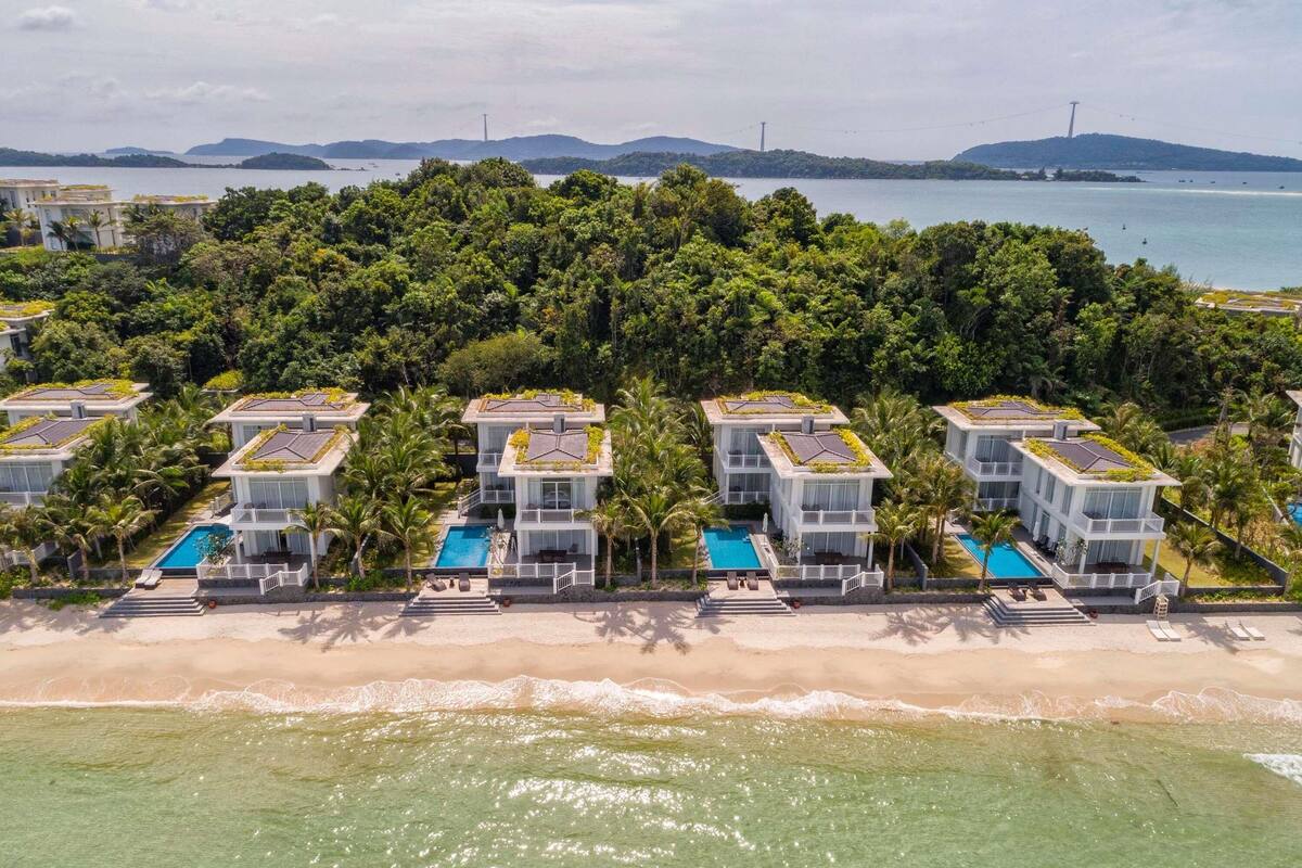 Ein Resort mit mehreren Gebäuden, jedes mit einem Dachpool, umgeben von üppiger Vegetation und einem Strand.