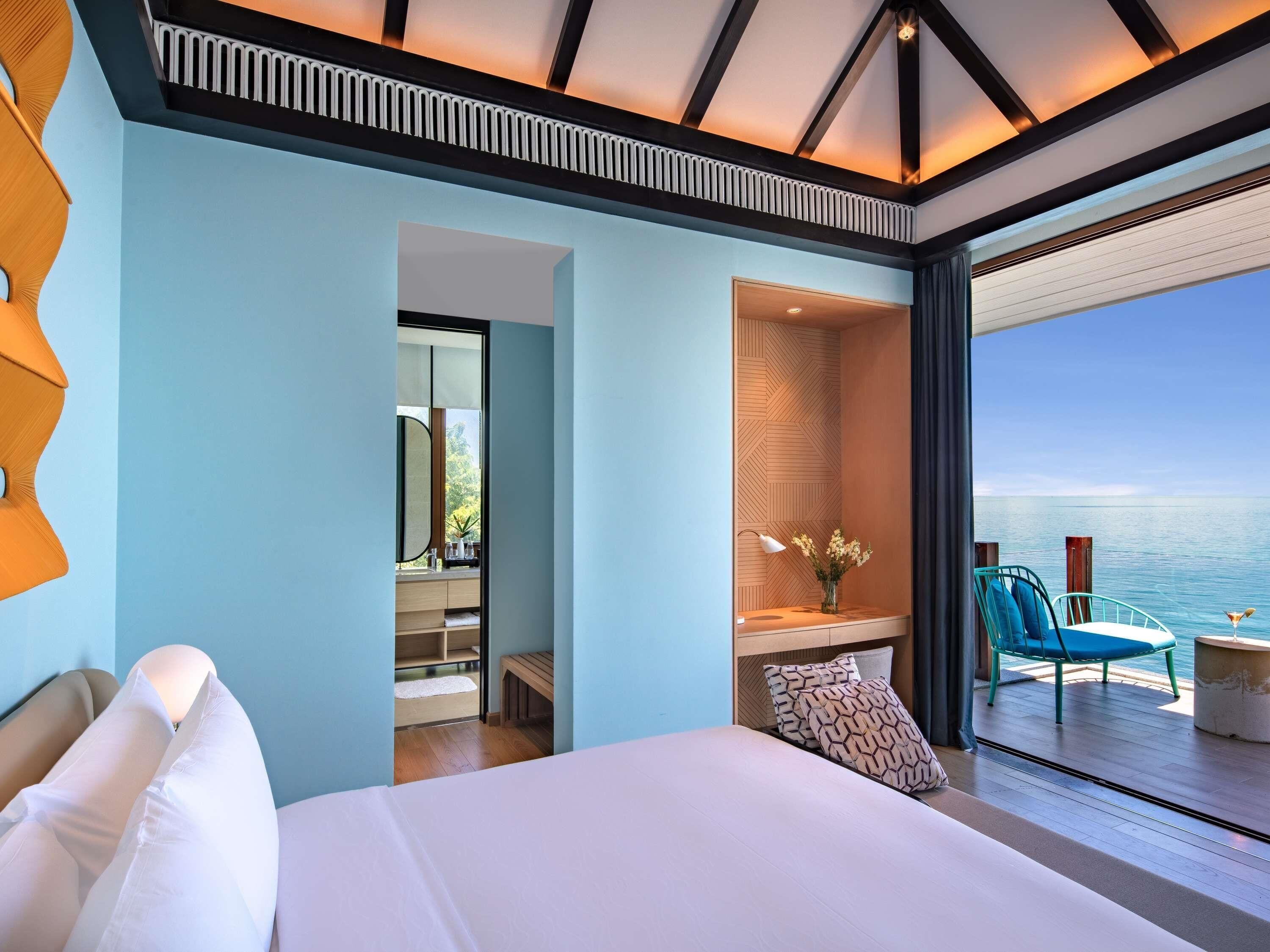 Una habitación de hotel moderna con una cama grande, un baño con espejo y tocador, y vista al mar.