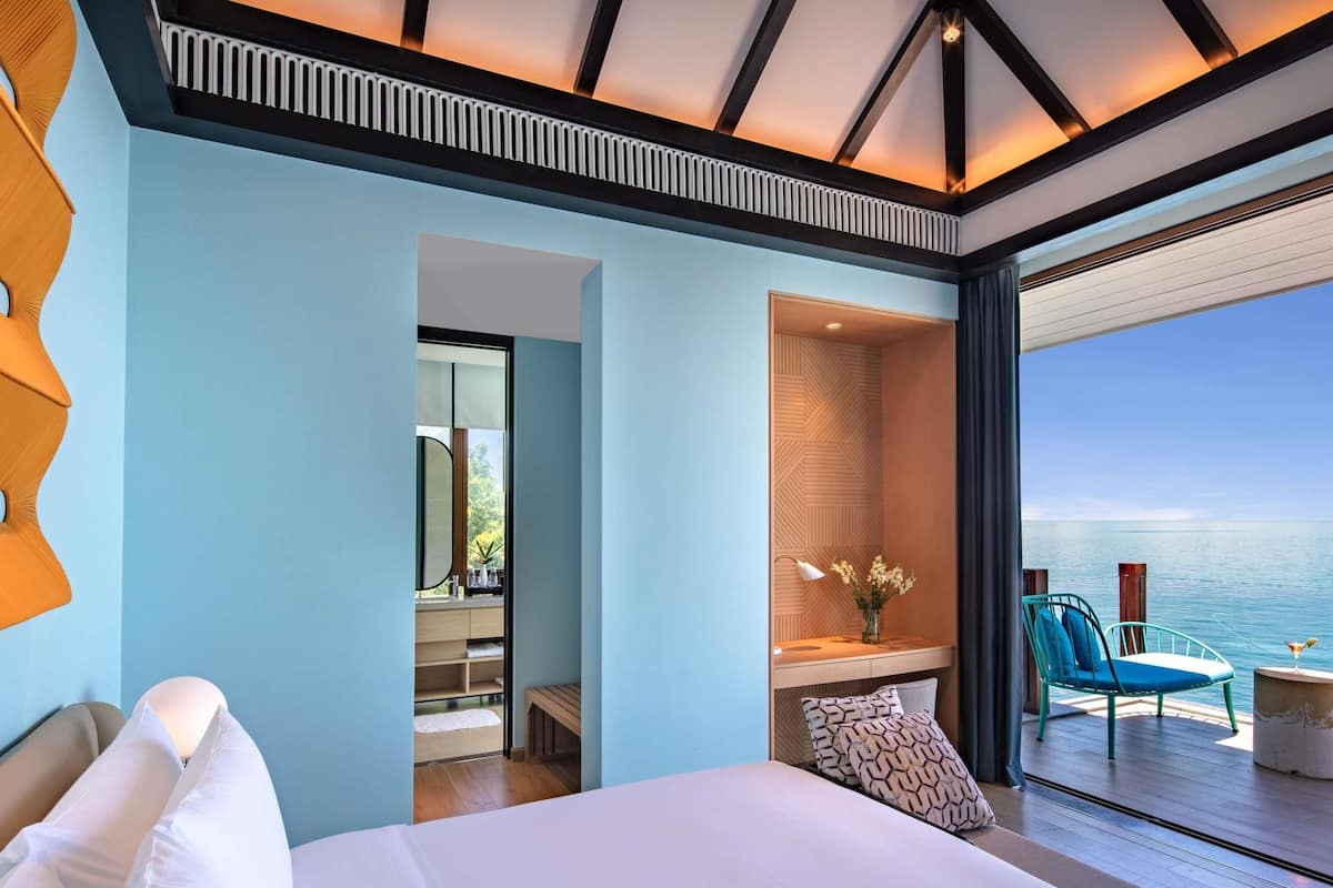 A modern hotel room with a large bed, a bathroom with a mirror, a vanity, and a view of the sea.