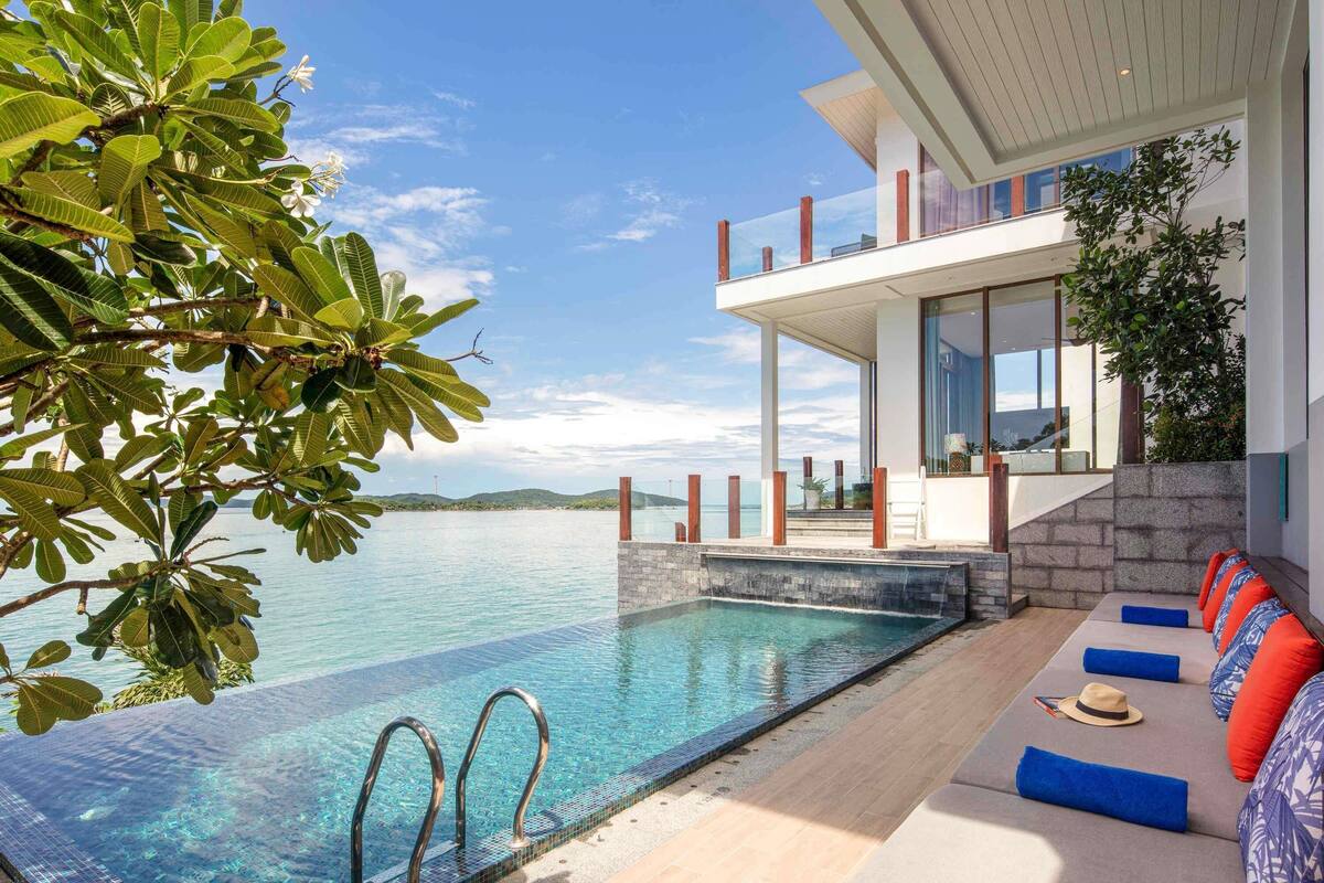 Ein moderner Poolbereich mit klarem Wasser, einer Holzterrasse und einer Lounge mit bunten Kissen.