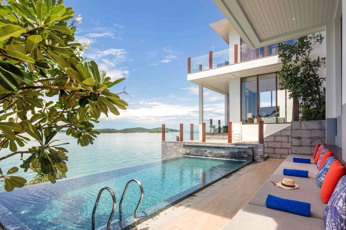 A modern pool area with clear water, a wooden deck, and a lounge with colorful cushions.