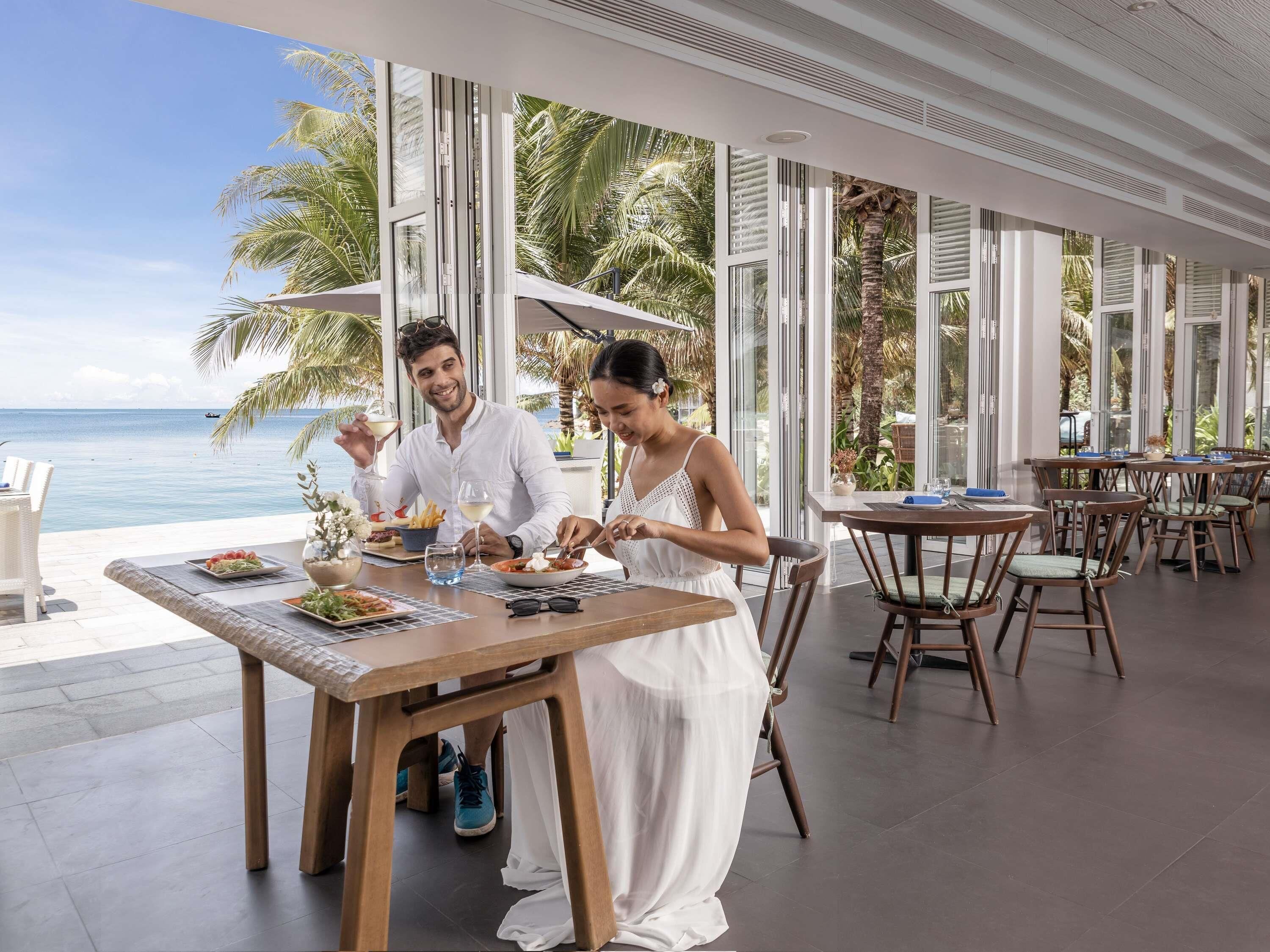 A dining area with a view of the ocean, large windows, and wooden furniture.