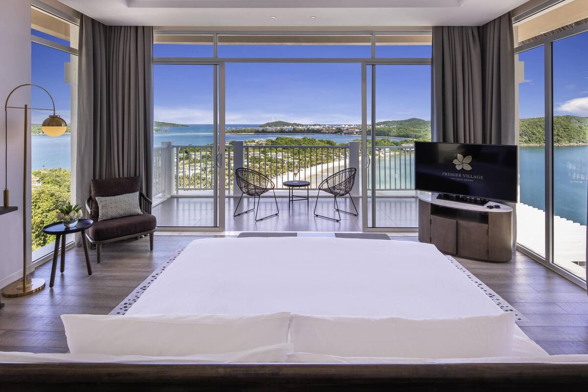 Ein geräumiges Schlafzimmer mit einem großen Bett, einem Fernseher und einem Balkon mit Blick auf das Meer und die Hügel.