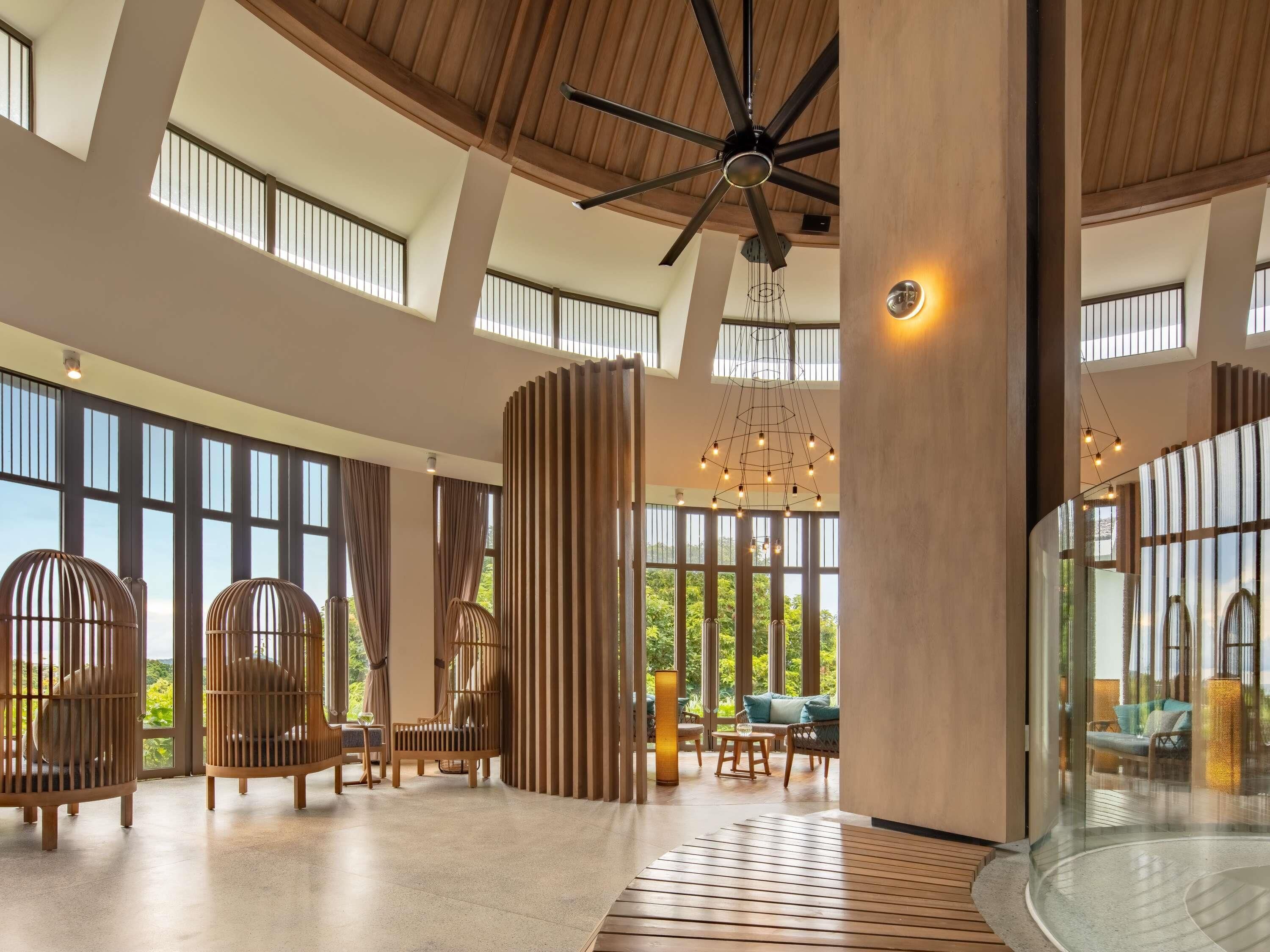 A spacious interior with high ceilings, large windows, and a central seating area with chairs and tables.