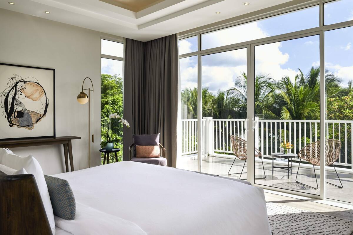 Ein Hotelzimmer mit einem großen Bett, Blick ins Freie, einem Balkon mit Stühlen und einem Bild an der Wand.