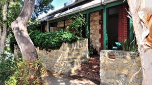 Un edificio rústico con un muro de piedra, una puerta verde y un sendero de ladrillo que lleva a la entrada.