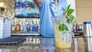 A bartender pouring a drink into a glass with ice and mint leaves.