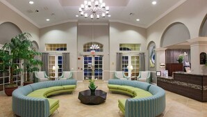 A spacious lobby with a central coffee table, green upholstered seating, and a reception desk.