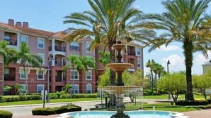 A multi-story building with balconies, a central fountain, and palm trees.