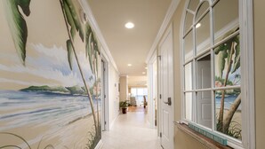 A hallway with a beach mural, a doormat, and a window with a view of palm trees.