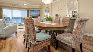 A dining area with wicker chairs, a round table, and a television on the wall.