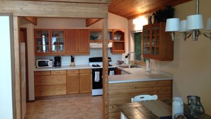 A kitchen with wooden cabinets, a microwave, a stove, and a dining area with a table and chairs. - Stunning Lake Views, Perfect U.P. Day-Trip Location, Day-Trip To Mackinac Island (St. Ignace)