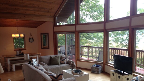 A spacious living room with a large window, a sofa, a coffee table, and a television. - Stunning Lake Views, Perfect U.P. Day-Trip Location, Day-Trip To Mackinac Island (St. Ignace)
