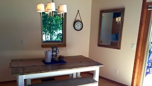A wooden dining table with a bench, a hanging light fixture, a clock, and a window with a view of greenery. - Stunning Lake Views, Perfect U.P. Day-Trip Location, Day-Trip To Mackinac Island (St. Ignace)