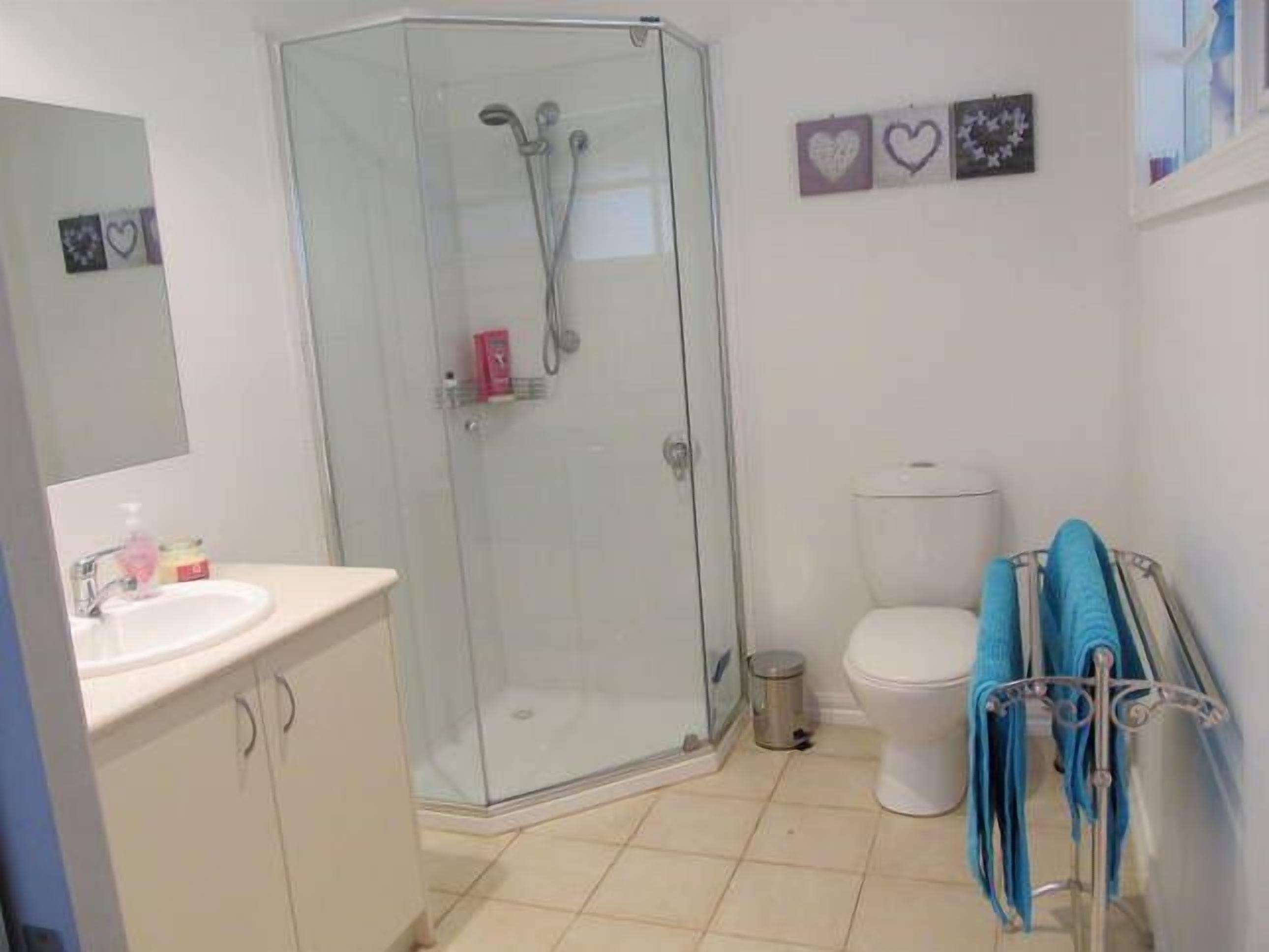 A bathroom with a glass-enclosed shower, a toilet, a sink with a mirror, and a towel rack with towels.
