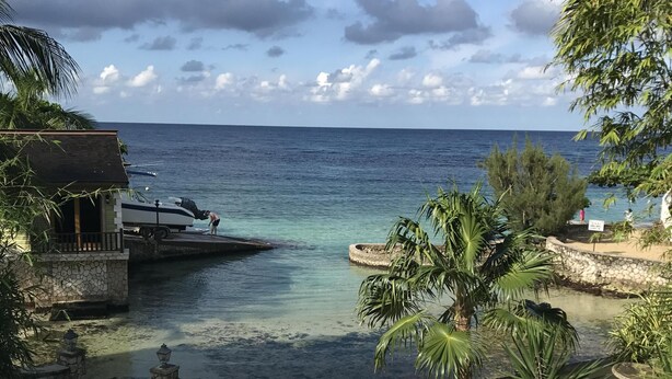 En pool med klart vatten, utsikt över havet och en liten brygga med en båt.