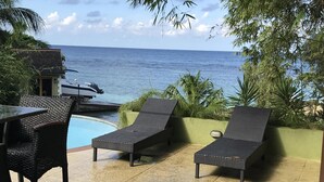 En uteplats med två solstolar och ett bord, med utsikt över en pool och havet.