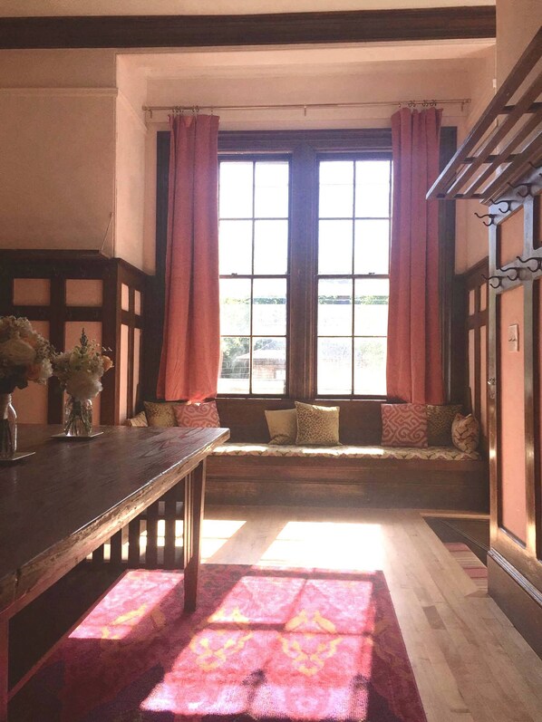 Une pièce avec un banc en bois, une table ornée d’un vase de fleurs et une fenêtre avec des rideaux.