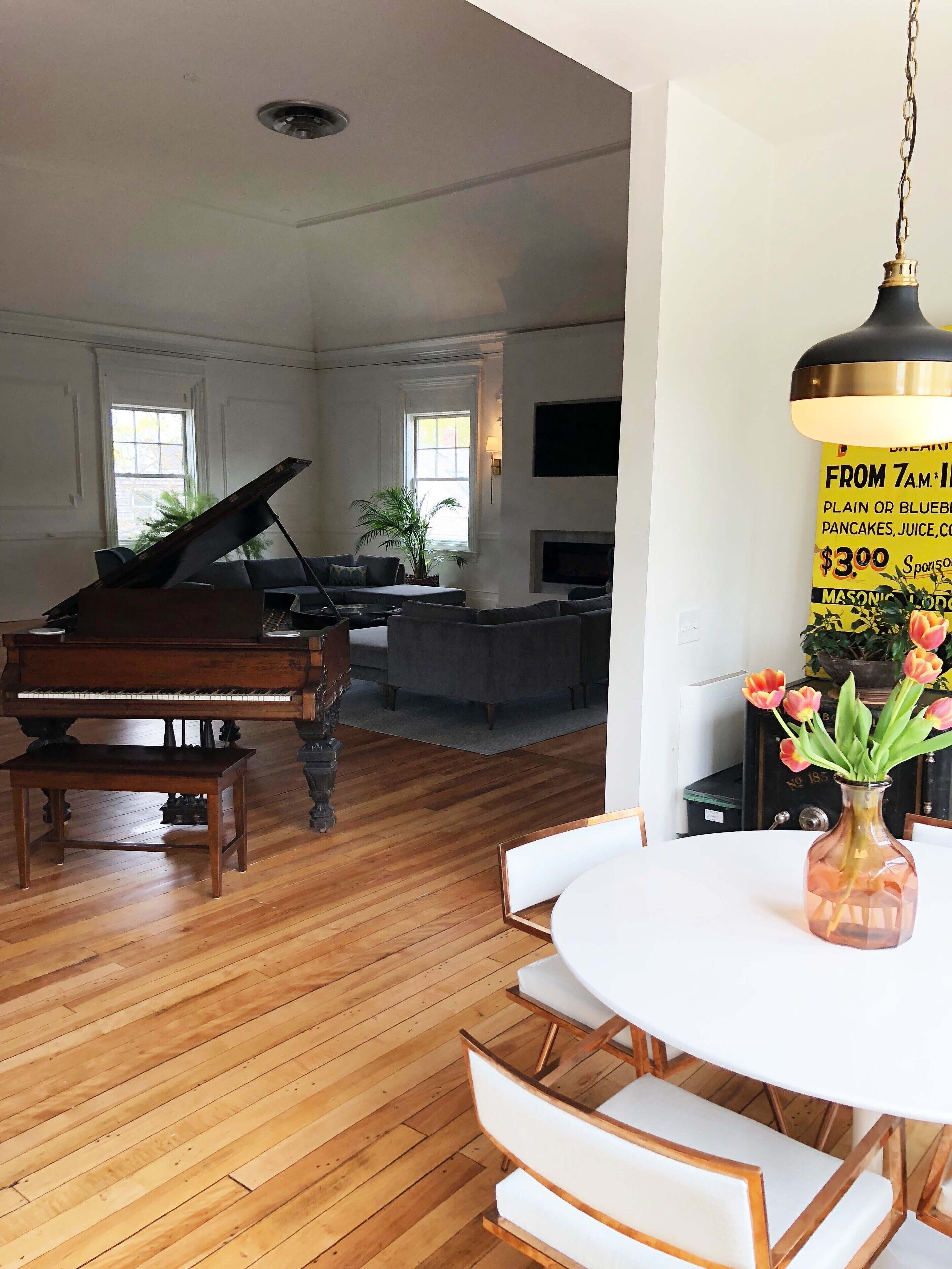Un vaste salon agrémenté d’un magnifique piano à queue, un coin repas avec une table ronde et des chaises, et une cuisine équipée d’un téléviseur à écran plat.