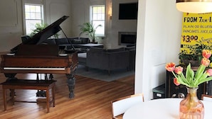 Ein geräumiges Wohnzimmer mit einem Flügel, einem Essbereich mit rundem Tisch und Stühlen sowie einem großen Fenster für natürliches Licht.