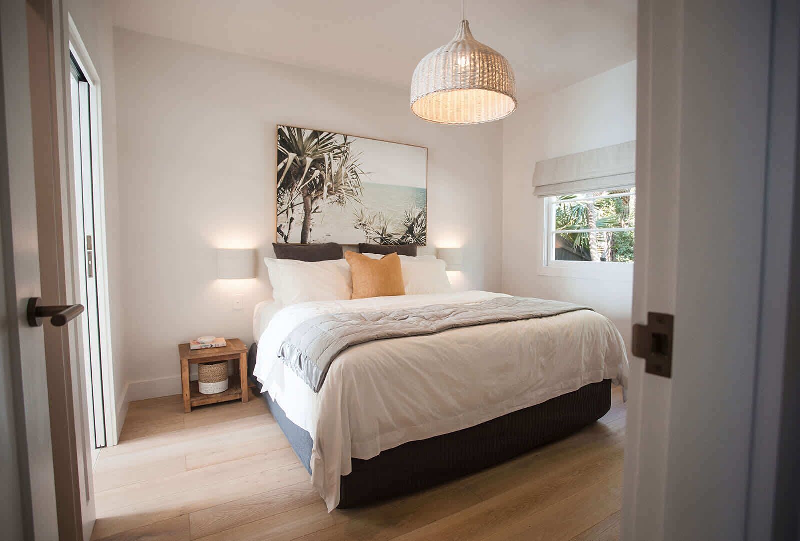 A bedroom with a bed, a bedside table, a hanging light fixture, and a window with a view.
