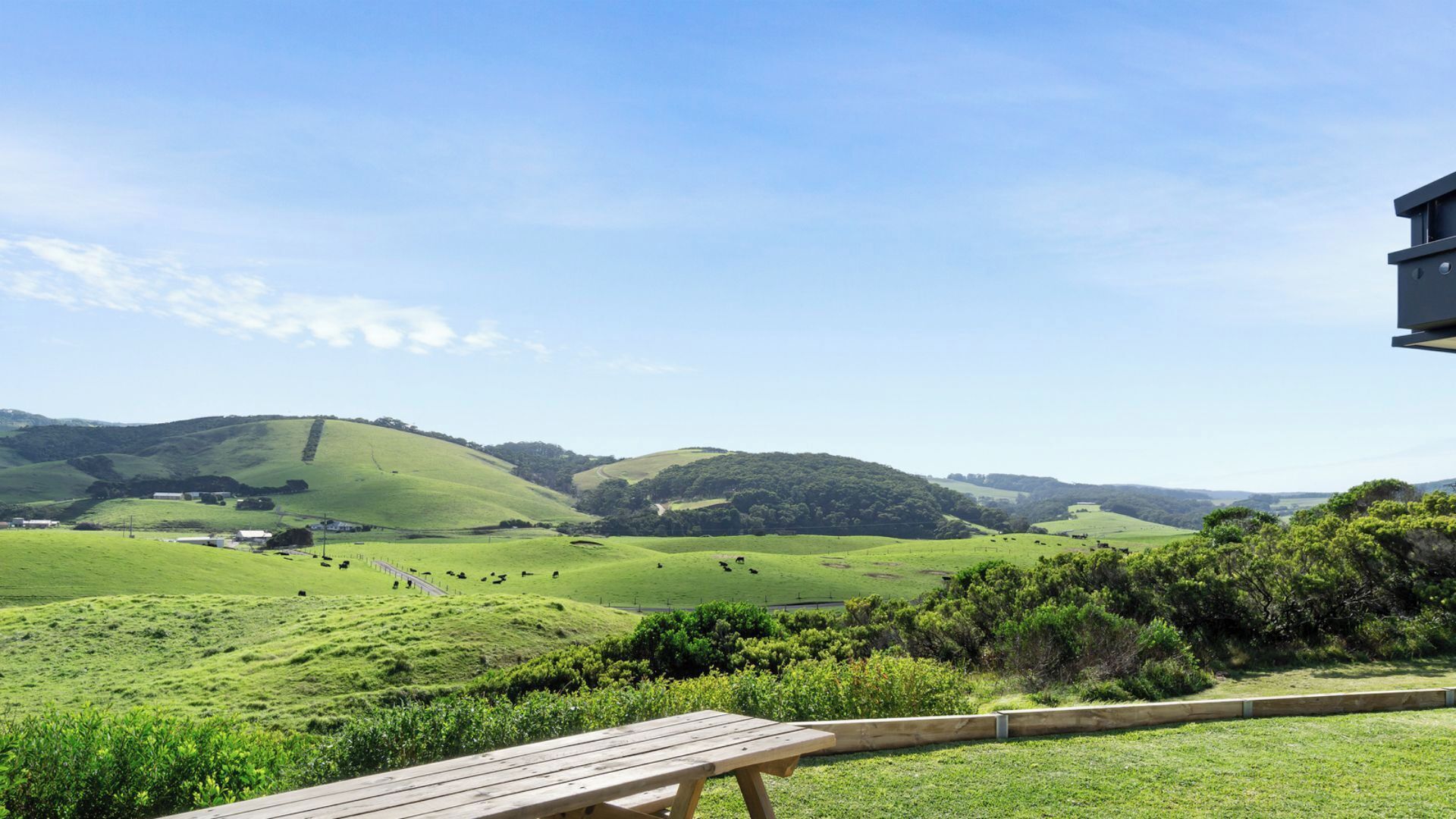 A scenic view of rolling green hills with a wooden deck and a building in the foreground.