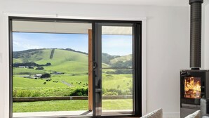A room with a sliding glass door leading to a countryside view, a fireplace, and a white wall. - Glen Tara Beach Retreat (Johanna)