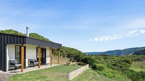 A modern house with a patio, outdoor seating, and a view of the surrounding hills. - Glen Tara Beach Retreat (Johanna)