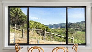 A dining area with a large window overlooking a mountainous landscape. - Glen Tara Beach Retreat (Johanna)