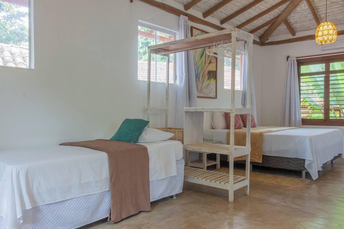 Une chambre avec deux lits simples, un banc en bois et un luminaire suspendu.