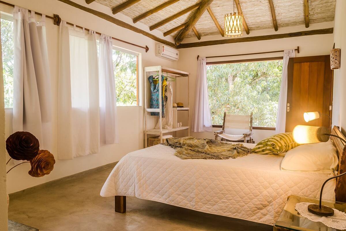Une chambre à coucher avec un lit, une chaise, une table avec une lampe et une fenêtre avec des rideaux.