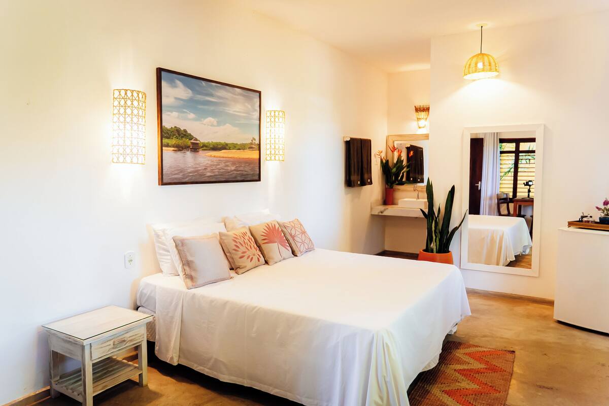 Une chambre à coucher avec un lit, des tables de chevet, un tableau, des appliques murales, un miroir et une plante en pot.