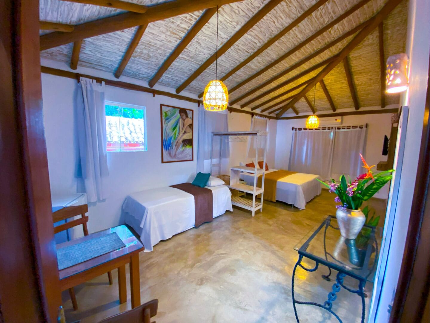 Ein gemütliches Zimmer mit Bett, Schreibtisch und Stuhl. Es gibt ein Fenster mit Vorhängen, ein Bild an der Wand und eine Pendelleuchte.
