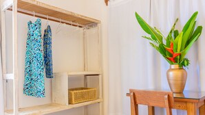 Une pièce comprenant une étagère en bois, une chaise, un vase avec une plante et un portant suspendu avec des vêtements à motifs.