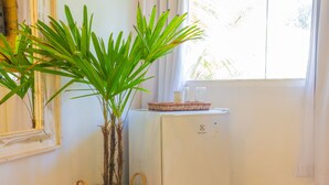 Une pièce avec un petit réfrigérateur blanc, un panier en osier et une plante en pot près d’une fenêtre.