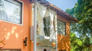 Une maison à deux étages, avec un toit en tuiles, de grandes fenêtres et des plantes en pot.