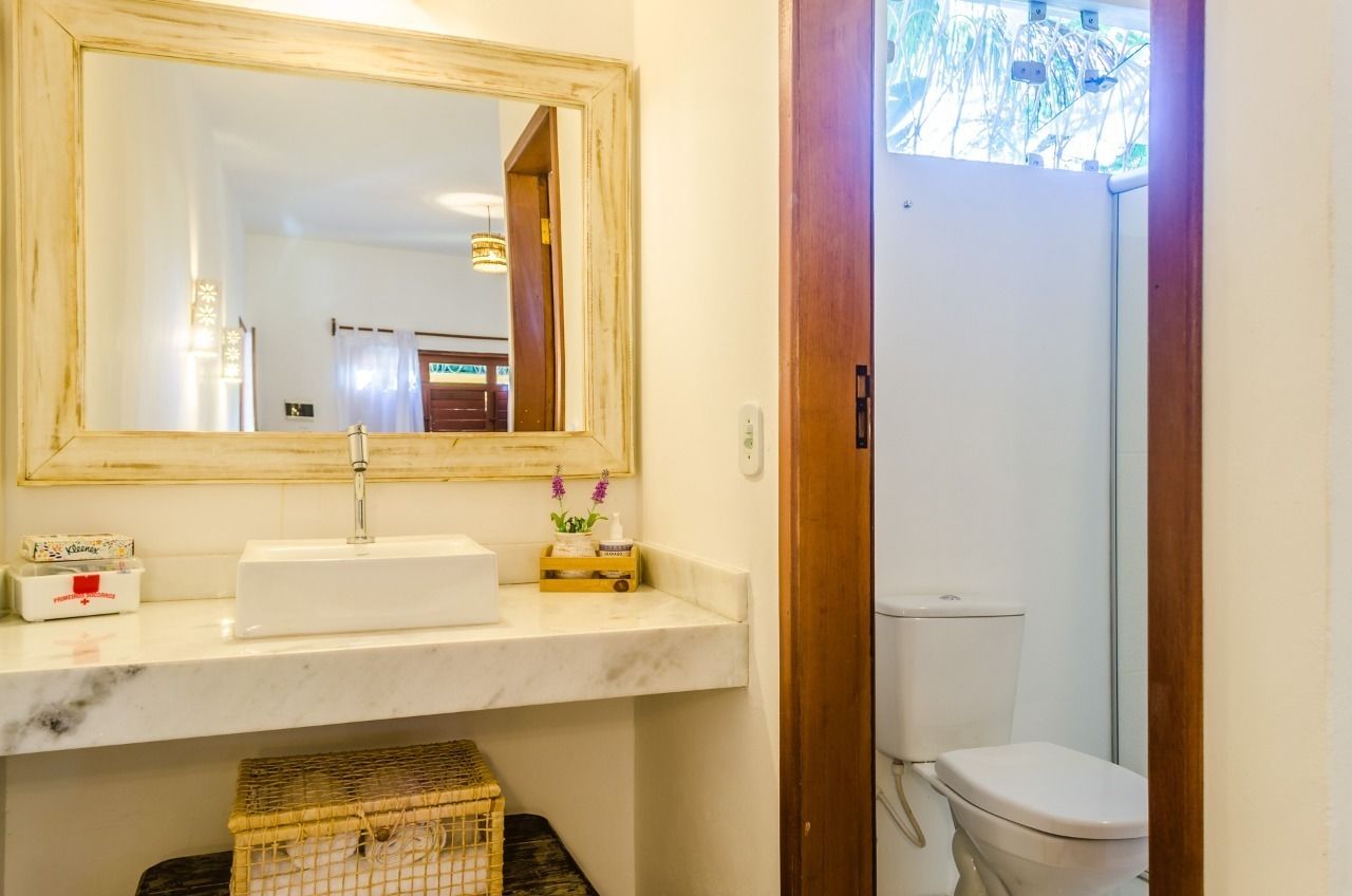A bathroom with a marble sink, a wooden-framed mirror, a toilet, and a wicker basket.