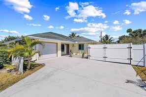 A single-story house with a garage, a covered driveway, and a white fence. - Citrus Cottage (Peggy's Retreat) (Hobe Sound)
