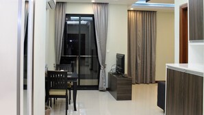 Una sala de estar moderna con comedor, televisor y un amplio ventanal con cortinas.