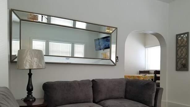 A living room with a grey sofa, a lamp, and a large mirror.