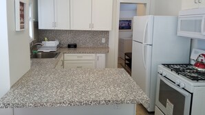 A compact kitchen with white cabinets, a granite countertop, a white refrigerator, and a gas stove.