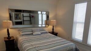A bedroom with a large mirror, a bed with striped bedding, two bedside lamps, and a window with blinds.