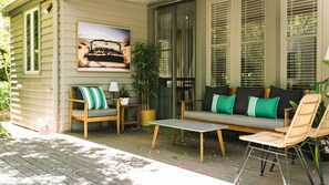 A covered porch with a wooden deck, a sofa set, a small table, and a chair.