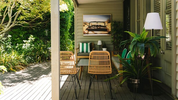 Une terrasse en bois avec des chaises et une table en osier, entourée de verdure et agrémentée d’une plante en pot.