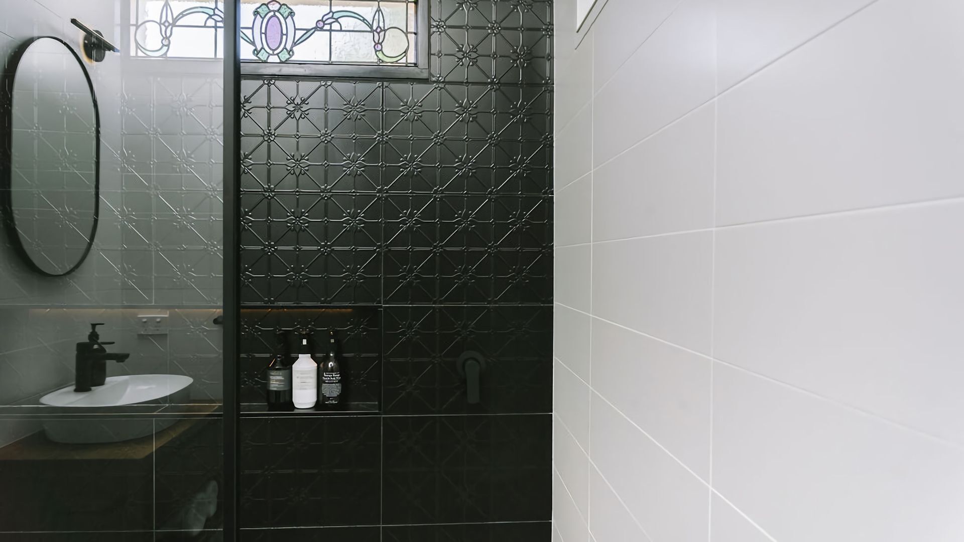 Een badkamer met een zwart betegelde muur, een wit wastafelmeubel en een spiegel.