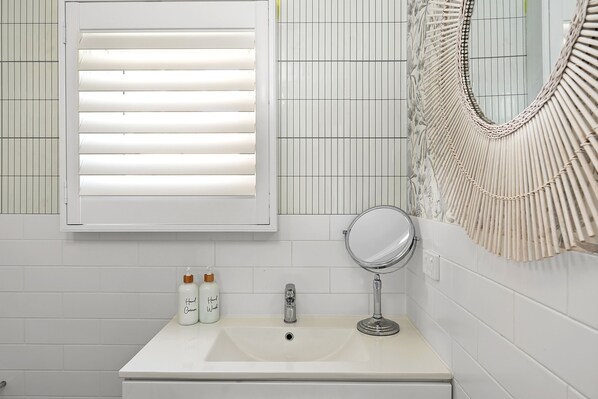 A bathroom with a white sink, a mirror, and a window with blinds.