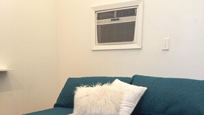 Un lit avec une couette et des draps de couleur turquoise et un oreiller moelleux blanc, un climatiseur fixé au mur et un interrupteur.